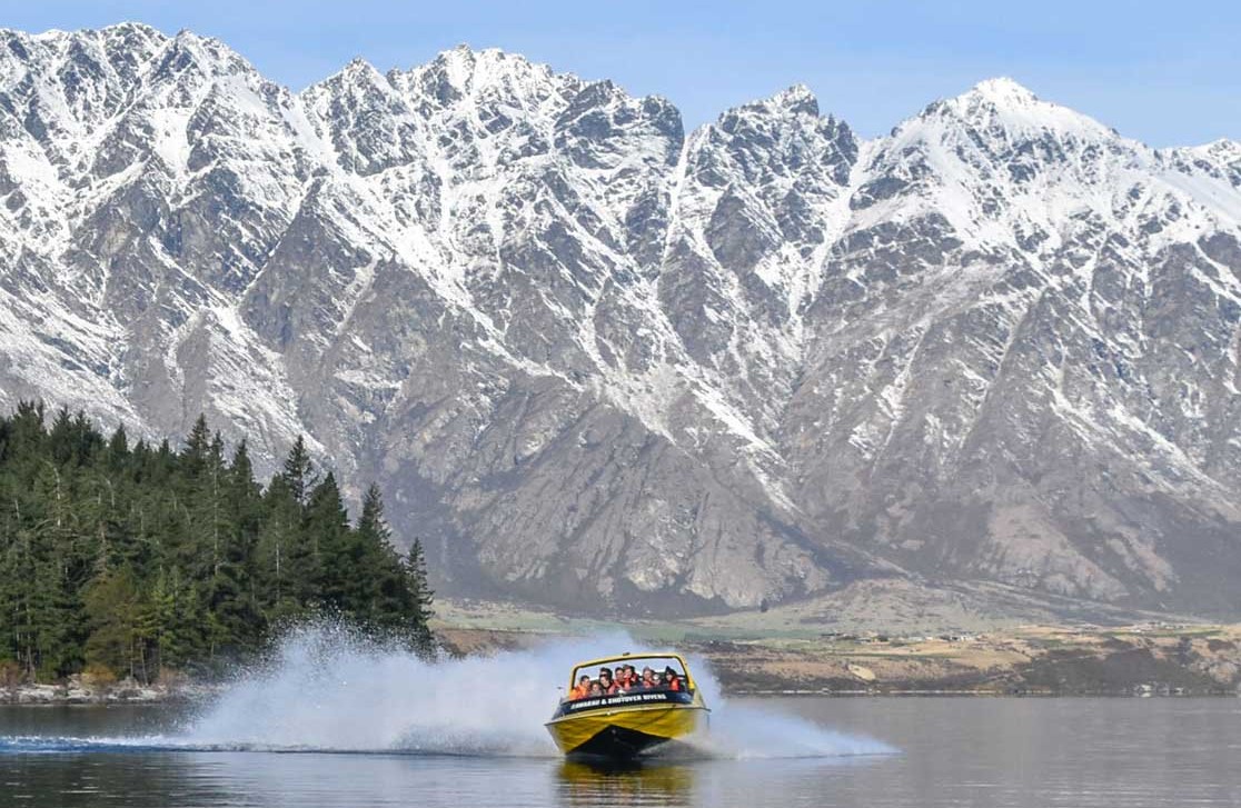 Group of people jet boating in winter on lake Wakatipu with lots of snow on the Remarkables mountain range with KJet Queenstown
